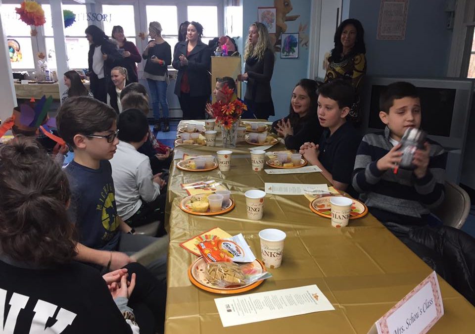 The full group of students, teachers, and parents sitting down together and eating their thanksgiving feast.